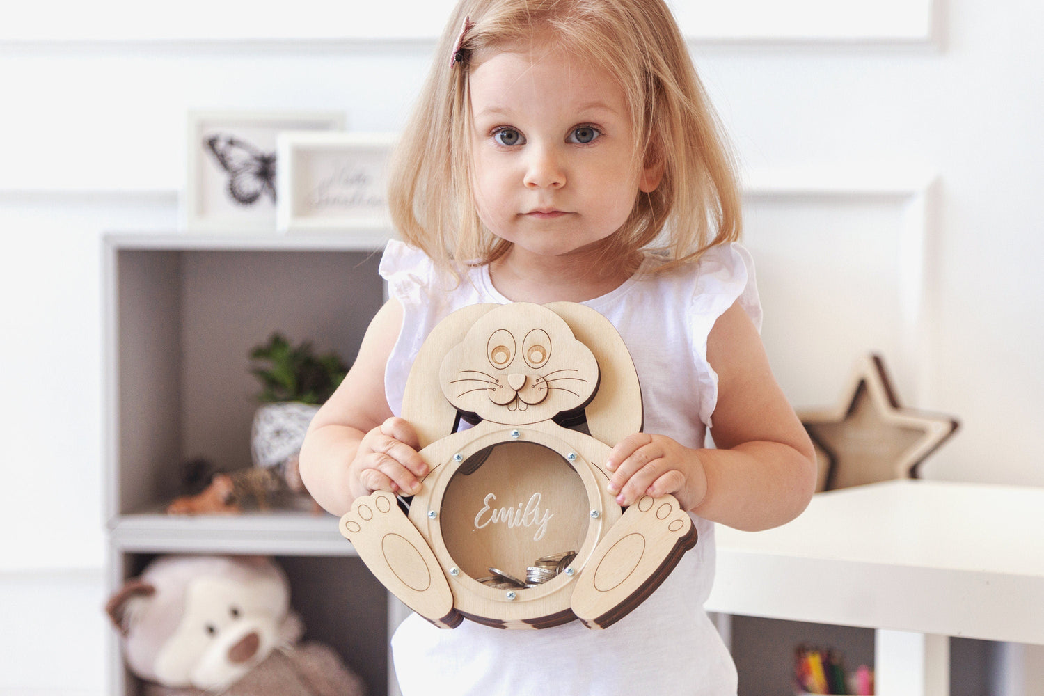 Little girl holding a personalized wooden bunny-shaped piggy bank with the name 'Emily', ideal for kids' savings and as a unique gift idea.