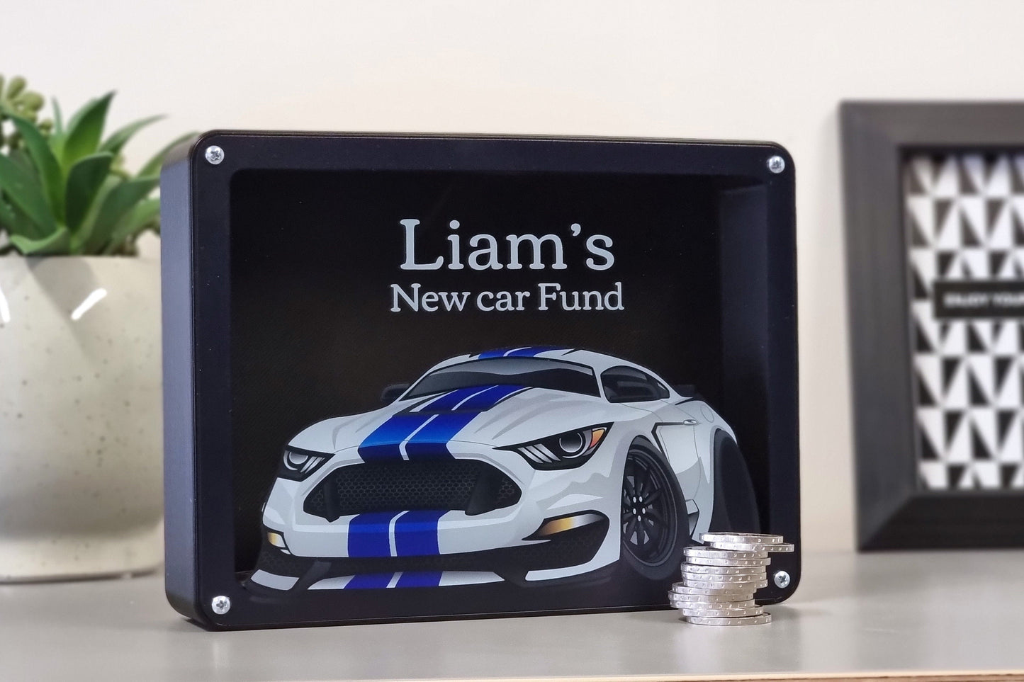 Blue car-themed personalized piggy bank on a table with coins.