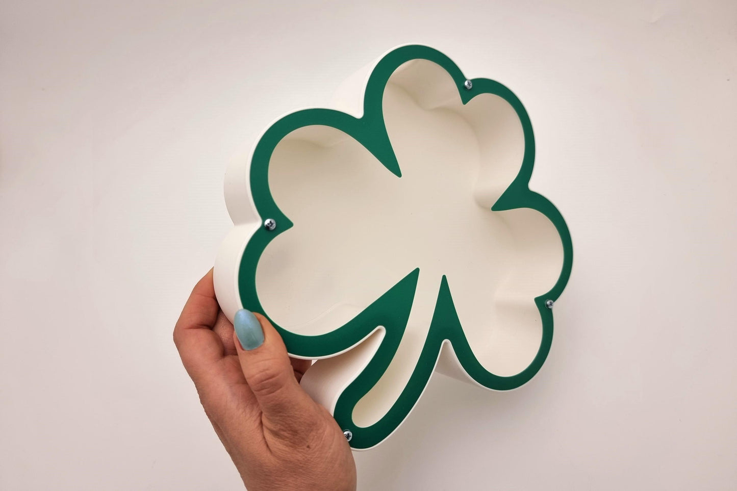 Hand holding green shamrock piggy bank, highlighting its lightweight and compact design.