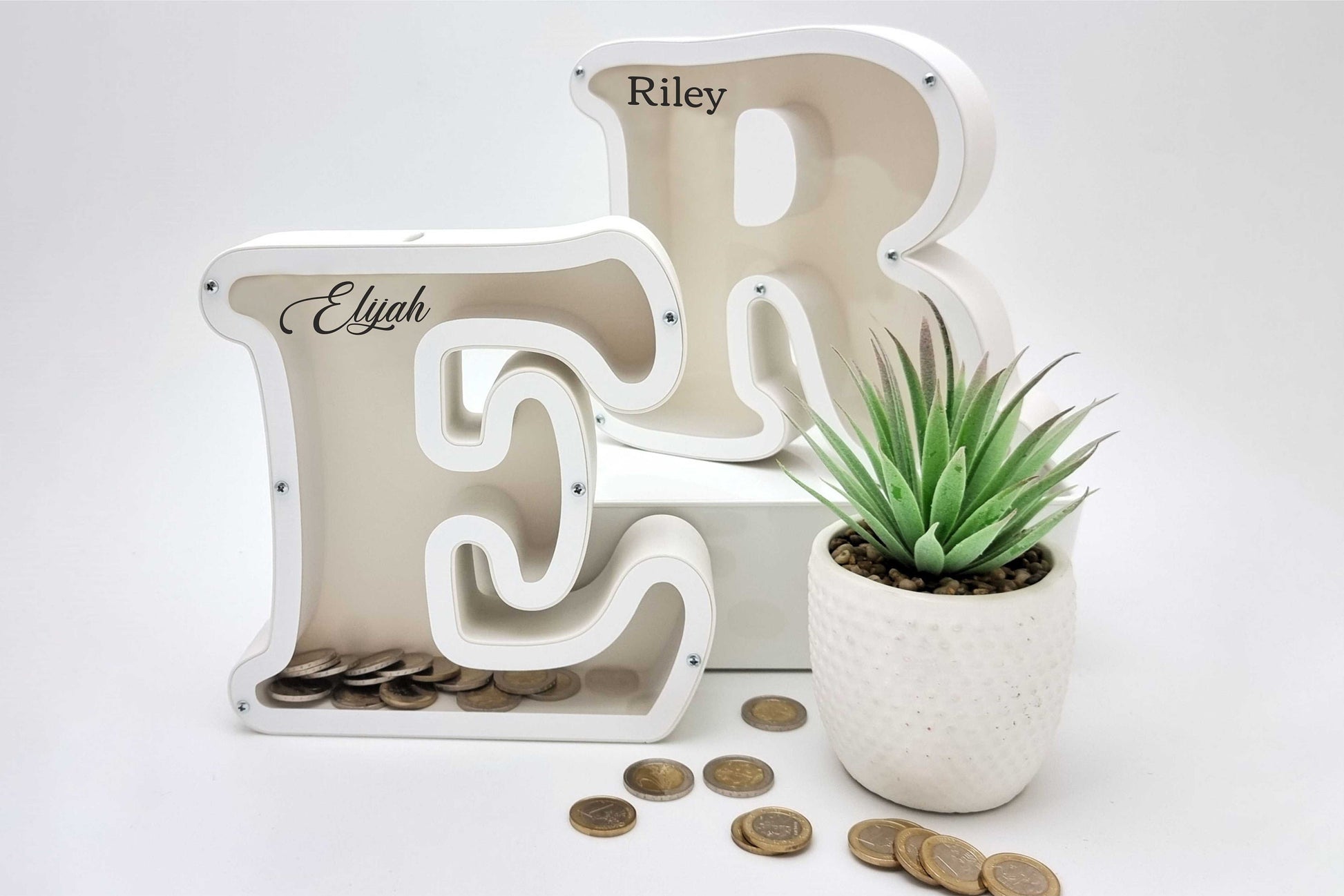 Personalized letters E and R piggy banks with coins next to flower, perfect gift for kids and adults.