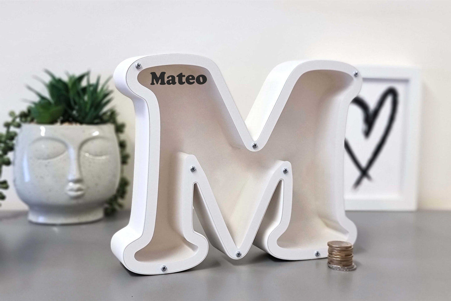 Personalized letter piggy bank M on a table, ideal for birthdays or special occasions.