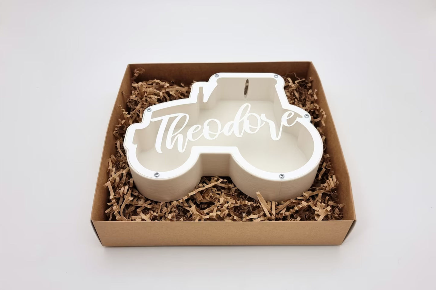 A white tractor-shaped piggy bank with "Theodore" engraving, neatly placed in an eco-friendly gift box, ideal for gifting on birthdays or special occasions.